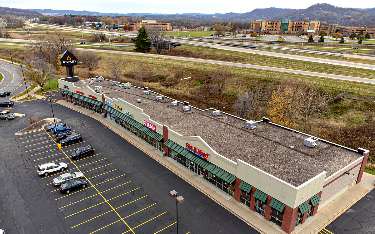 Aerial view of a single-story strip center and its parking lot beside a highway